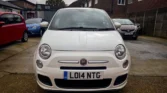 Front view of a white Fiat 500 parked on a driveway with other cars visible in the background.