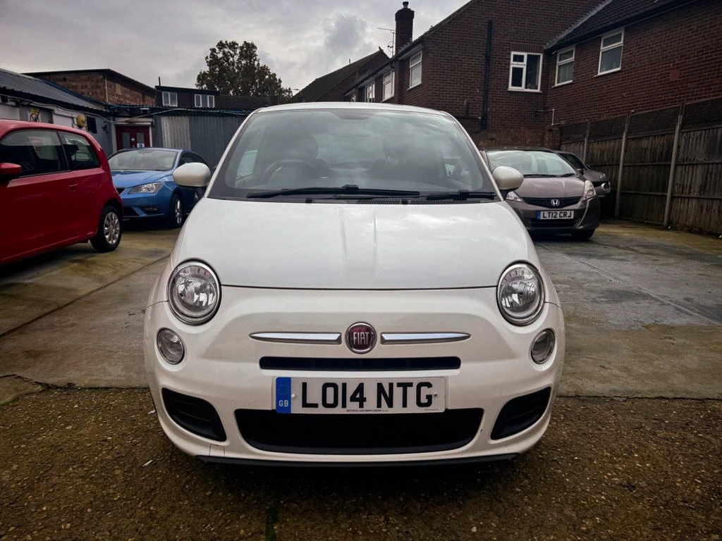 Front view of a white Fiat 500 parked on a driveway with other cars visible in the background.