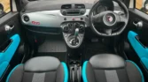 Interior view of a Fiat 500, showing black and turquoise sport seats, dashboard, and steering wheel. Right-hand drive setup.