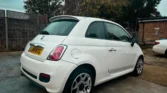 Rear quarter view of a white Fiat 500 showing its distinctive alloy wheels parked on a driveway.